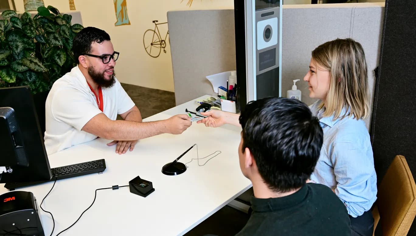 Man and woman sitting at a desk in the INAmsterdam offices, employee handing over an id card