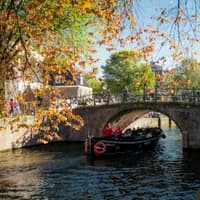A tour boat passing by under the bridge on a sunny autumn day on Reguliersgracht.