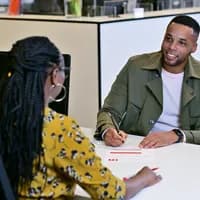 Man sitting at the desk in the INAmsterdam offices, seen from the front, talking to employee, seen from the back