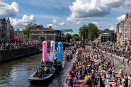 A crowd of people on the streets and in a boat with flags and signs - Pride Canal Parade