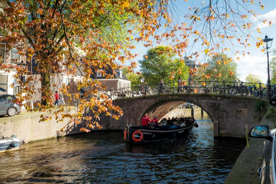 A tour boat passing by under the bridge on a sunny autumn day on Reguliersgracht.