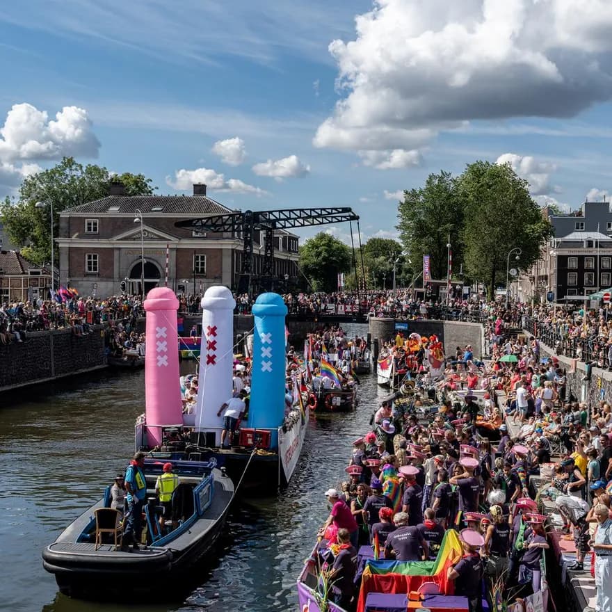 A crowd of people on the streets and in a boat with flags and signs - Pride Canal Parade