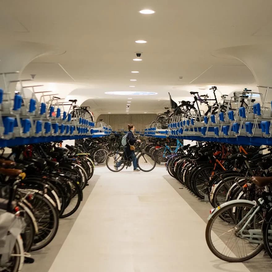 Woman walking through the underground bike parking with a bike in her hand. On de sides bicycle storages