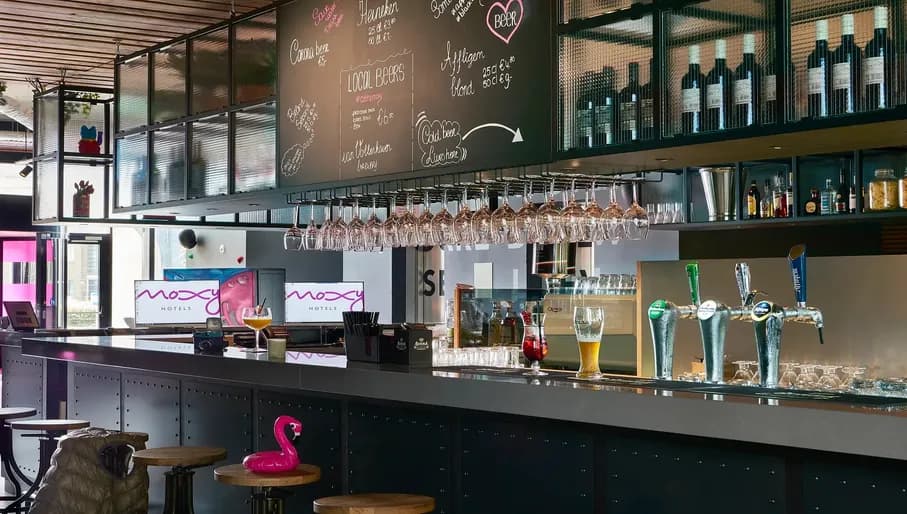 Bar of Moxy Amsterdam Schiphol Airport hotel, with chalkboard, beer taps and glasses of half-finished drinks on counter.