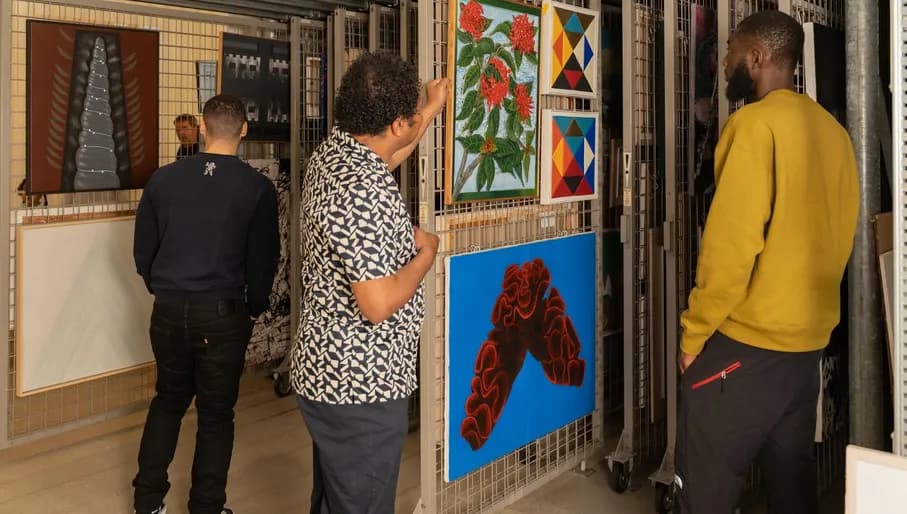 Two men listen to the story of a museum employee during their visit to the art loan of CBK Zuidoost.
