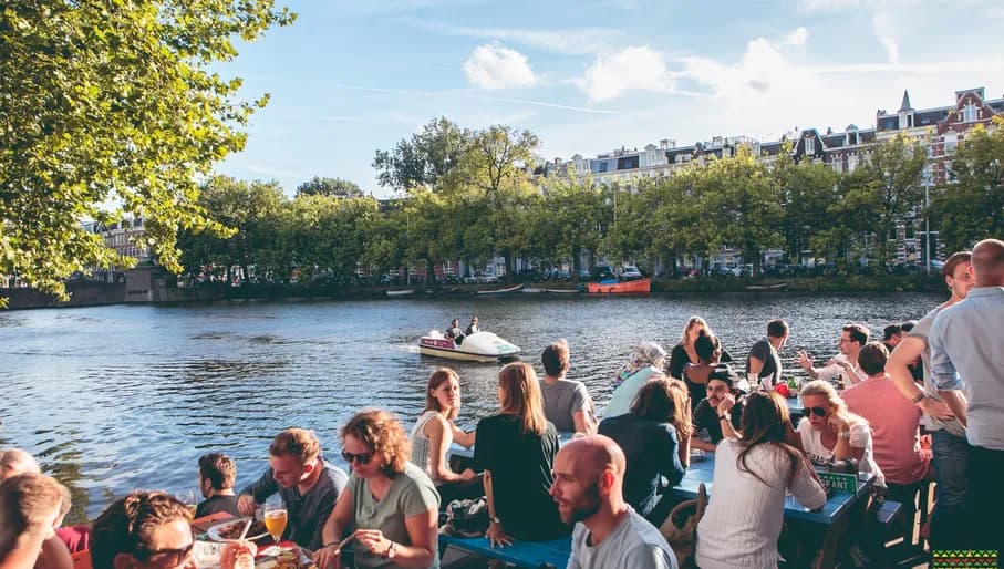 Waterkant people sitting on the terrace next to the water and a water bike passing by