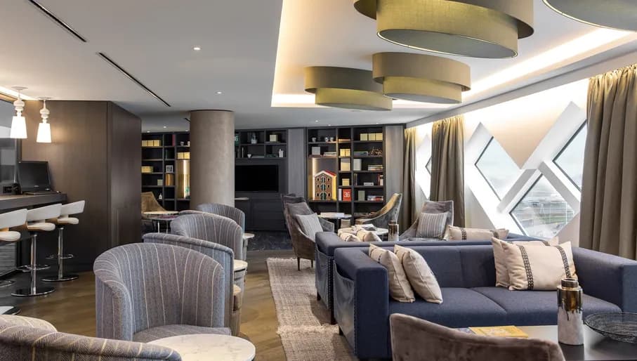 Lounge of Amsterdam Schiphol Airport hotel including sofas and chairs with airport visible through windows.