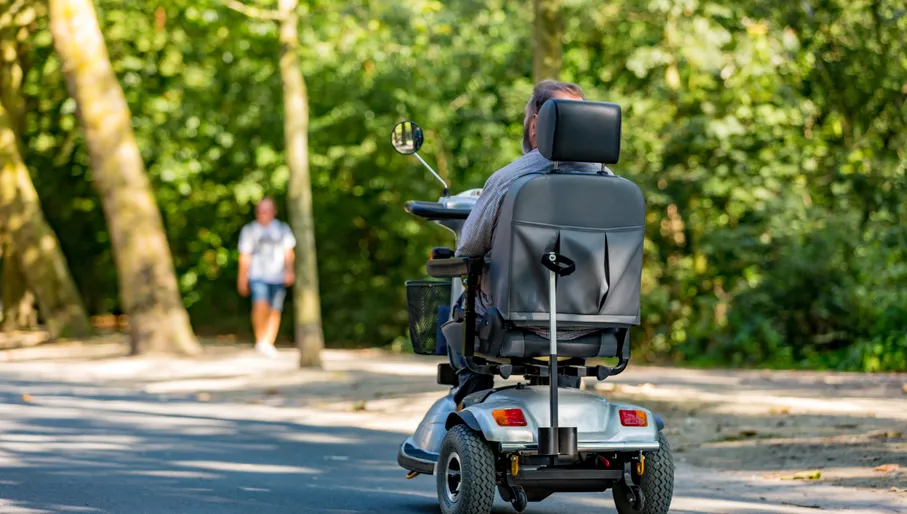 A older man riding in an electric wheelchair in a sunny and green Amsterdam Vondelpark in the Netherlands.